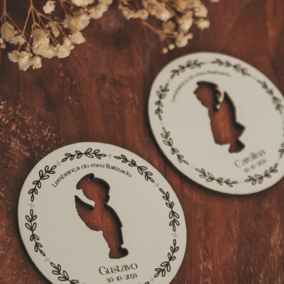 Lembranças de batizado redondas em madeira clara com recorte de criança a rezar e texto decorativo