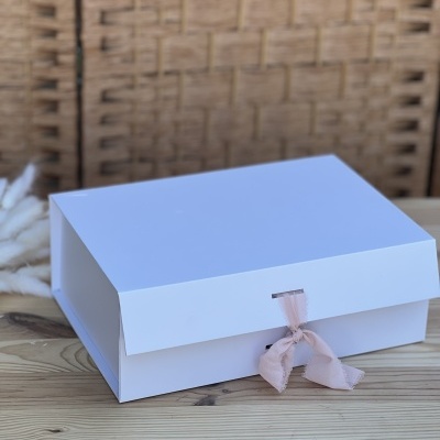 Caixa branca com fecho de fita rosa em superfície de madeira.