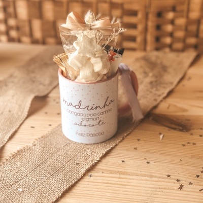 Caneca decorativa com arranjo dentro sobre mesa de madeira e tecido bege.