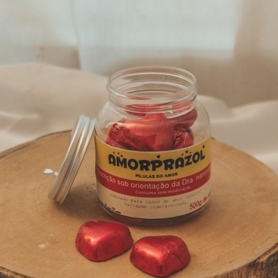 Frasco plástico com balas vermelhas metálicas em forma de coração sobre base de madeira