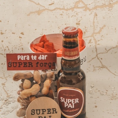 Frasco de cerveja, pacote de amendoins e bilhete com texto em português num cenário claro e envelhecido