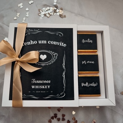 Caixa de convite com chocolates e laço dourado sobre fundo bege com confetes