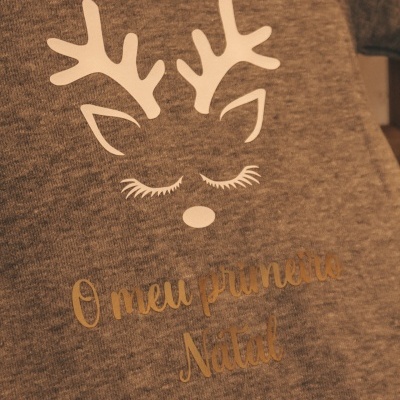 Camisola cinzenta com estampa de rena branca e texto dourado 'O meu primeiro Natal'.