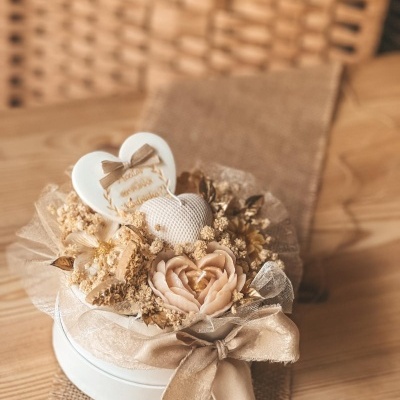 Arranjo decorativo com caixa branca, flores secas, velas em forma de coração e flor, e laço bege