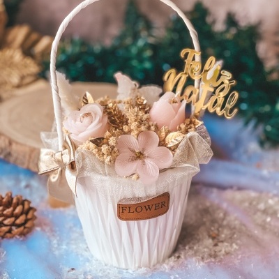 Cesto branco com flores artificiais cor-de-rosa e placa dourada 'Feliz Natal'.