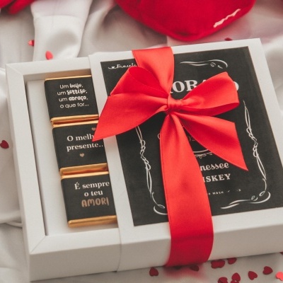 Caixa de presente com barras de chocolate e laço vermelho sobre tecido branco com corações vermelhos