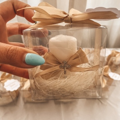 vela branca com laço bege e cruz em embalagem plástica transparente