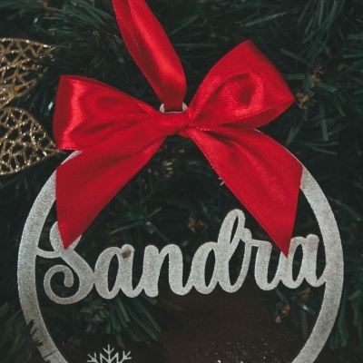 Decoração natalícia prateada com nome Sandra e laço vermelho pendurada na árvore