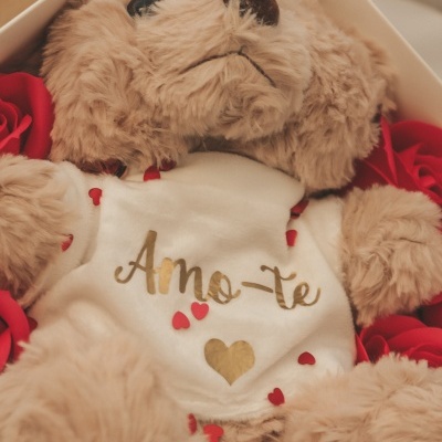 Urso de peluche castanho claro com t-shirt branca 'Amo-te' numa caixa com rosas vermelhas.
