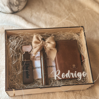 Kit em caixa de madeira com caneta, carteira e chaveiro em couro castanho rodeados por palha