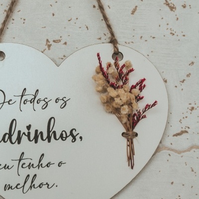Placa decorativa branca em forma de coração com texto em português e ramo de flores secas