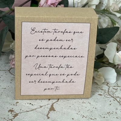 Caixa de cartão com etiqueta rosa e texto preto rodeada por flores sobre superfície manchada