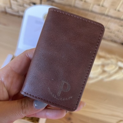 Carteira pequena de couro castanho com símbolo e costura à vista numa mão.