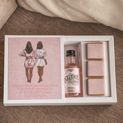 Caixa de presente com mini garrafa de gin e chocolates em papel rosa com texto em português.