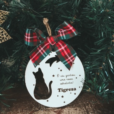 Etiqueta redonda branca com laço xadrez e silhueta preta de gato pendurada na árvore de Natal.