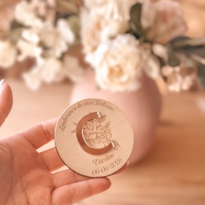 Brinco C em metal rose gold em base de madeira com gravação floral e texto sobre batismo