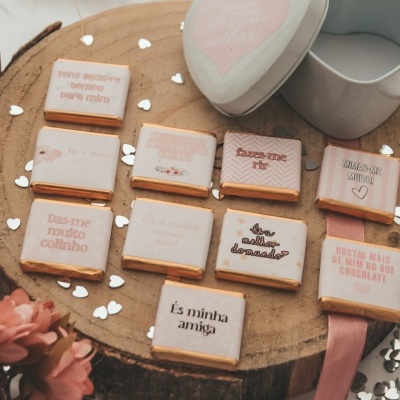 Gomas de chocolate com mensagens gravadas em rosa e branco sobre suporte de madeira redondo.