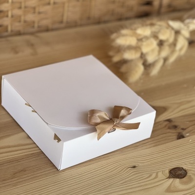 Caixa branca com laço castanho claro sobre madeira clara
