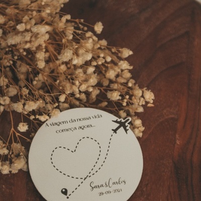 Base redonda branca com texto e desenho de avião sobre madeira e flores secas