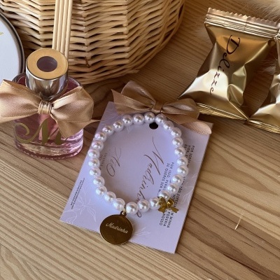 Pulseira de pérolas com pendente dourado e frasco de perfume com laço sobre mesa de madeira