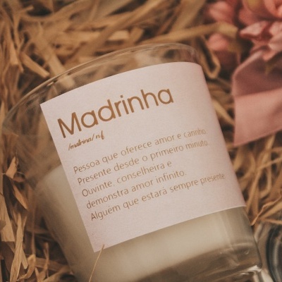 Vela branca em copo de vidro com etiqueta rosa clara e texto em castanho