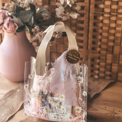 Saco de plástico transparente com alças bege e decoração de margaridas, com etiqueta de Feliz Páscoa madrinha