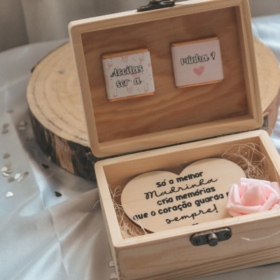 Caixa de madeira com pedra decorativa e texto, decorada com saquinho rosa, sobre tecido prateado
