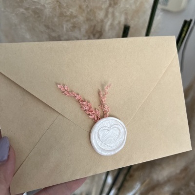 Envelope bege com selo de cera branco e raminhos secos cor-de-rosa