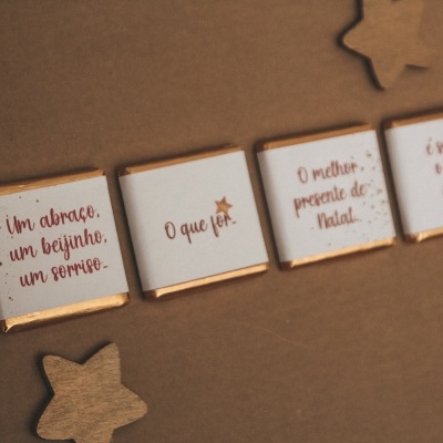 Quatro chocolates quadrados com mensagens em português e estrelas de madeira no fundo castanho