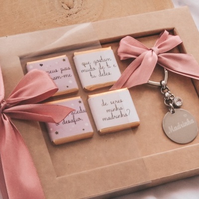 Barras de chocolate em embalagens cor de rosa e creme, chaveiro cinza 'Madeleine', laços rosa em caixa de papel kraft