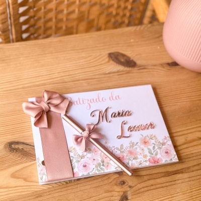 Cartão de batizado decorado com laços cor de rosa e flores, texto Batizado da Maria Leonor numa mesa de madeira