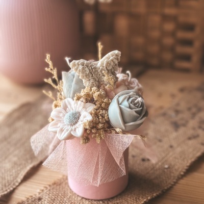 Arranjo de flores artificiais em caixa rosa com tecido e flores pastel sobre mesa de madeira.