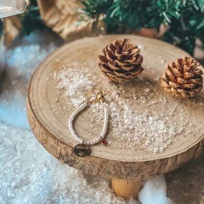 Pulseira de pérolas com pendente dourado e pinhas sobre base de madeira com neve artificial