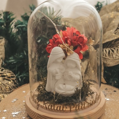 Escultura de presépio branca sob redoma de vidro com base de madeira e flores vermelhas