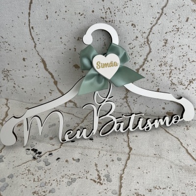 Cabide branco decorativo com texto 'Meu Batismo' e laço verde com coração escrito 'Simão'