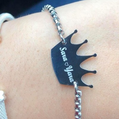 Pulseira prateada com pendente em forma de coroa e texto gravado no pulso