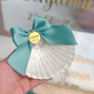Concha decorativa com laço turquesa e pendente dourado com texto Benjamin 22-08-2026