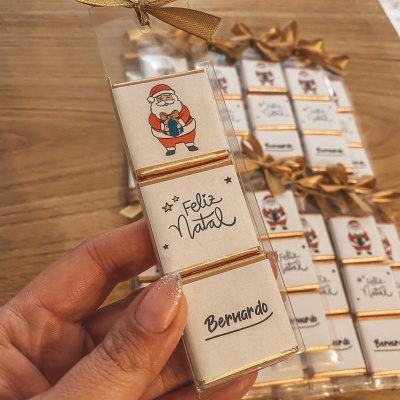 Caixa transparente com três chocolates e laço dourado, decorada com Pai Natal, 'Feliz Natal' e nome Bernardo.
