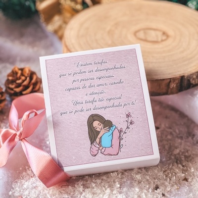 Caixa com cartão rosa e laço em ambiente com neve artificial e pinhas.