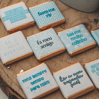 Pequenos chocolates quadrados embalados em papel colorido com textos em português sobre superfície de madeira