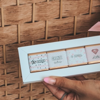 Moldura branca com três ilustrações e textos segurada por mãos femininas com unhas pintadas de rosa