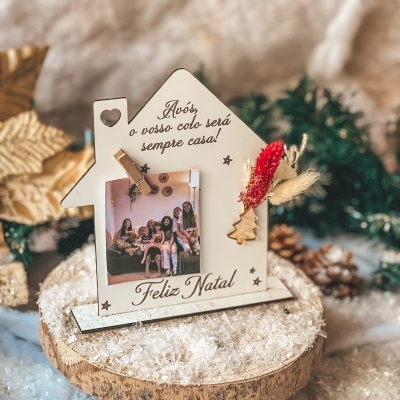 Moldura de madeira em forma de casa com mensagem natalícia, foto e decoração seca colocada numa base de madeira com neve artificial.