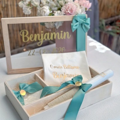 Conjunto para batismo com vela branca, fitas azul-turquesa, tecido com texto dourado e moldura de vidro com texto amarelo.