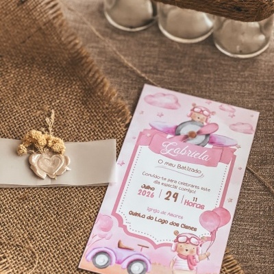 Convite de batizado rosa com ursinho e avião sobre tecido de juta com selo de cera e flor seca