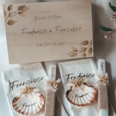 Caixa de madeira com texto gravado e dois conjuntos de toalhas com nomes e decoração com conchas e velas.