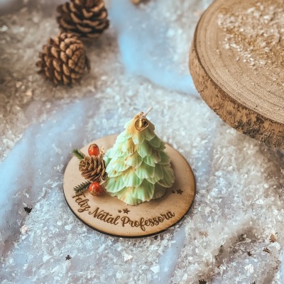 Vela árvore de Natal verde com sino dourado sobre base de madeira com texto e decoração natalícia.