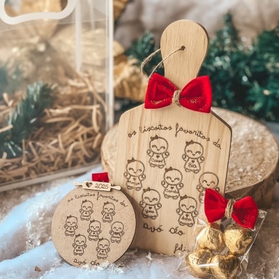 Decoração de Natal em madeira clara com ilustrações de bebés e laços vermelhos, com chocolates dourados embalados em plástico