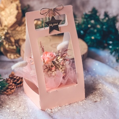 Arranjo de flores secas em caixa rosa com etiqueta de estrela e texto Feliz Natal