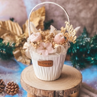 Cesta branca com flores artificiais e placa 'Feliz Natal' em decoração natalícia.
