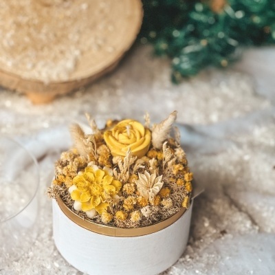 Vela amarela decorativa em caixa branca redonda com vegetação seca amarela e bege